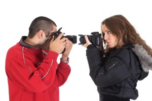 Young man and woman taking pictures of each other in front of the white background